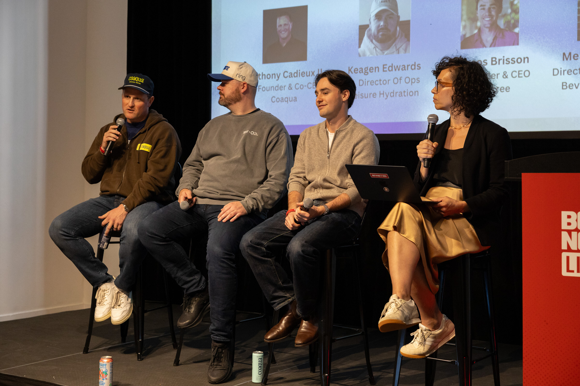 Four panelists on stools with microphones, one in a Coaqua cap, in front of a speaker slide.
