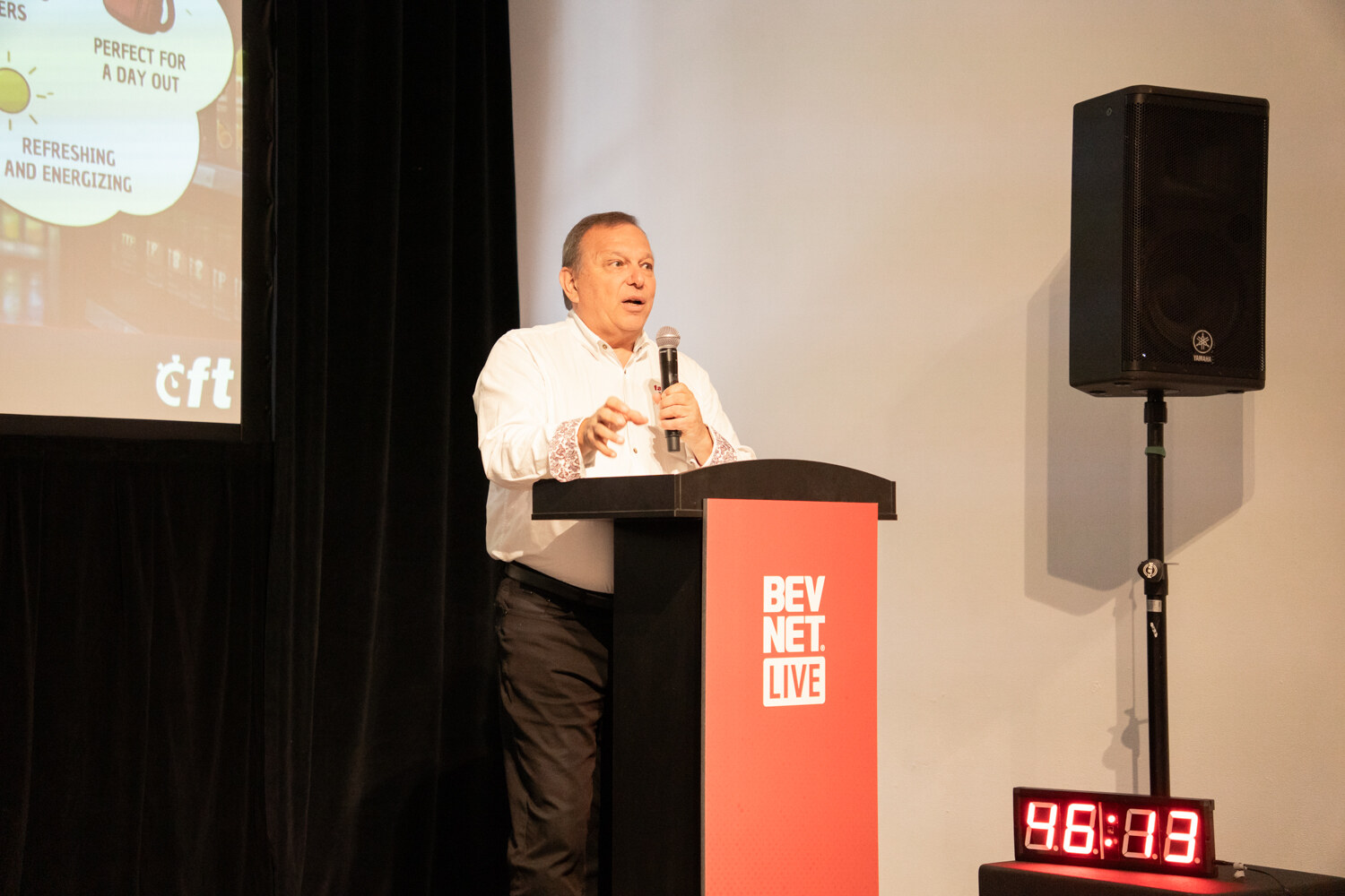 Man in a white shirt speaking at a red BevNET Live podium beside a loudspeaker and a red countdown timer.