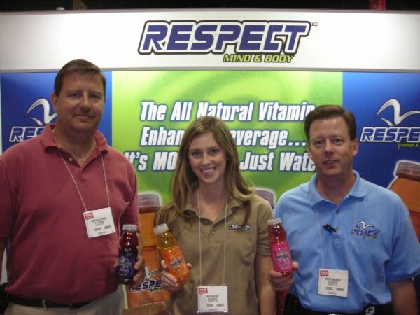 Two men and a woman stand in front of a Respect Mind & Body banner, each holding a bottle of flavored vitamin-enhanced beverage.