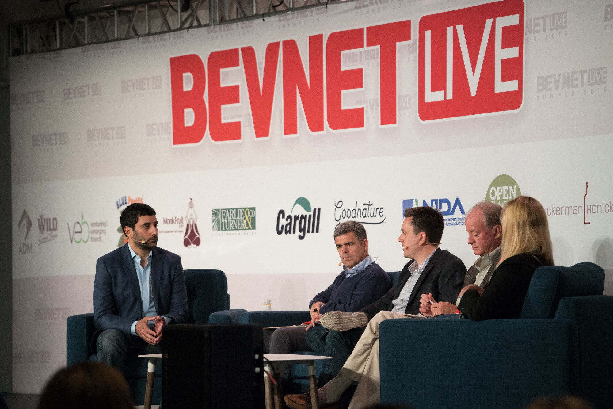 Wide view of a stage with a moderator in a navy blazer in one chair and four panelists on sofas under a red BevNET Live sign and sponsor logos including Cargill, Goodnature and Farlie & Turner.