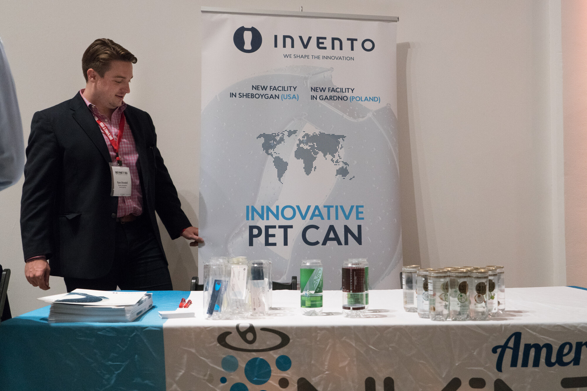 Man in a dark blazer beside an Invento banner reading Innovative PET Can, with clear sample cans and brochures on a blue and white table.