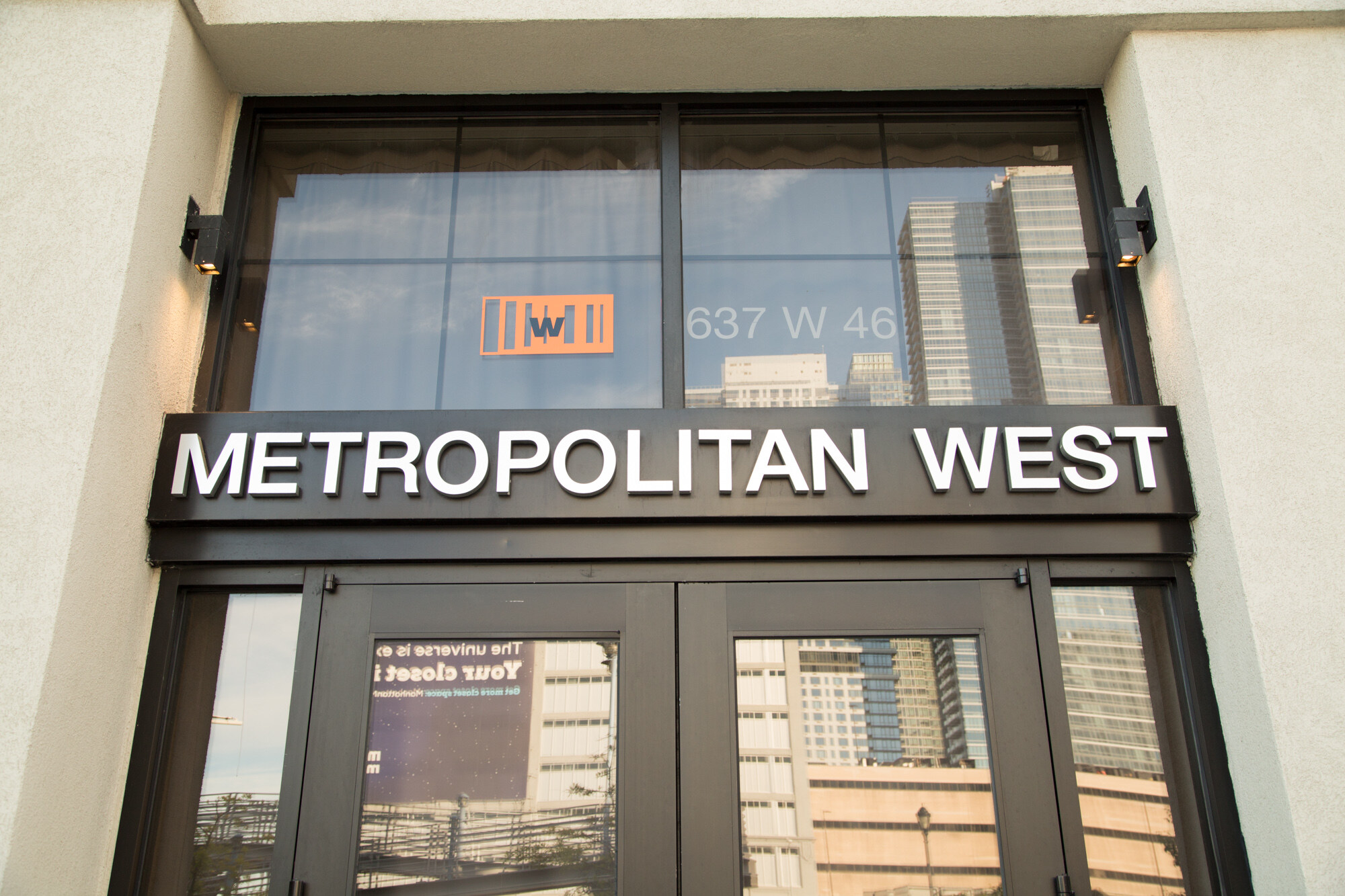 Glass entrance doors beneath a sign reading Metropolitan West, with 637 W 46 on the window above and city buildings reflected in the glass.