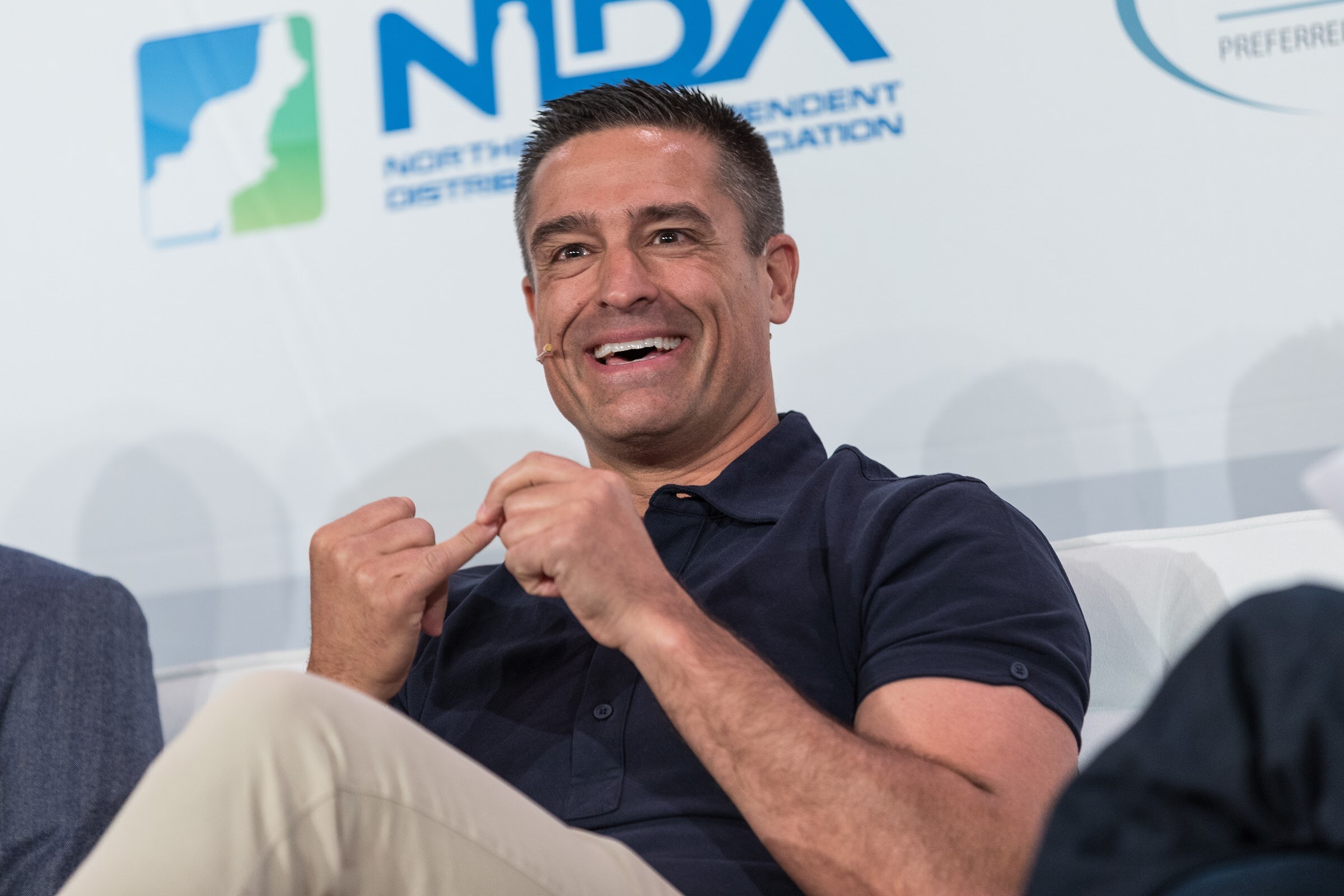 Close view of a man in a navy polo laughing with his hands together in front of a NIDA logo.