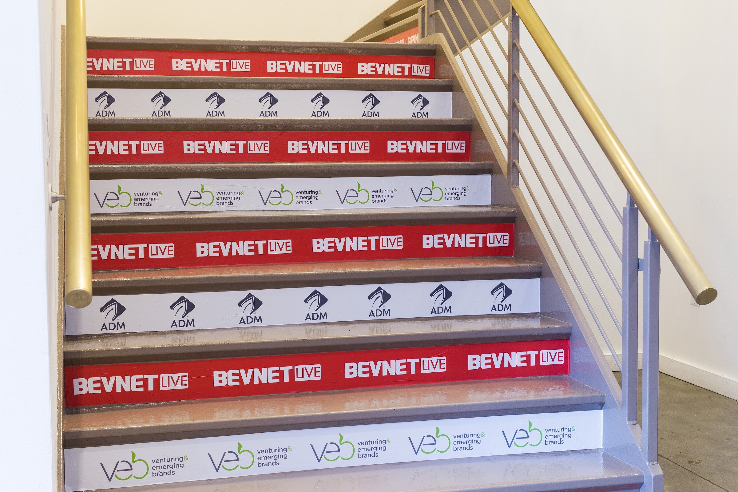 A staircase whose risers alternate red BEVNET LIVE bands, white ADM bands and white VEB venturing and emerging brands bands.