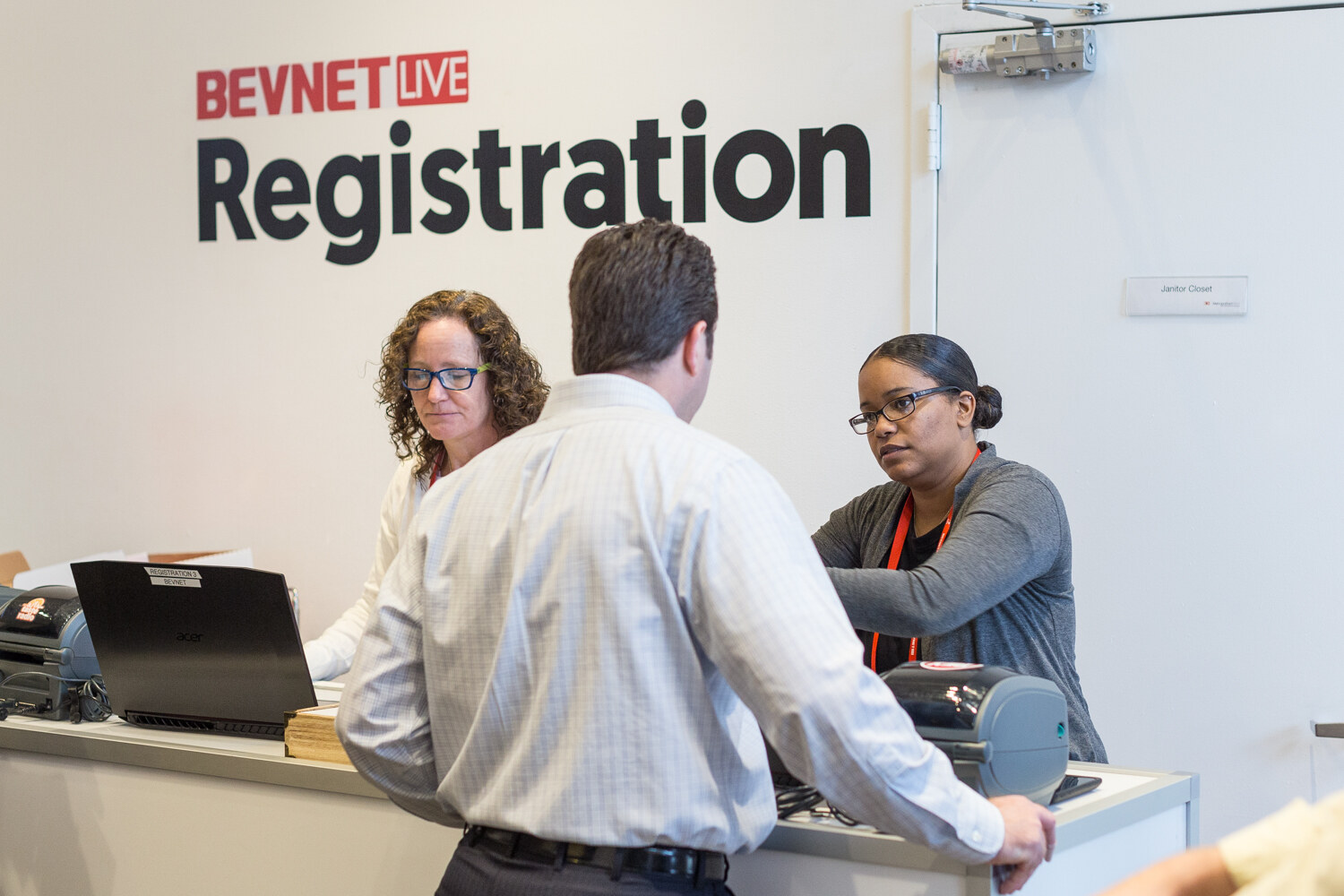 A man at a counter below a BevNET Live Registration sign talks with two women staffing the desk.