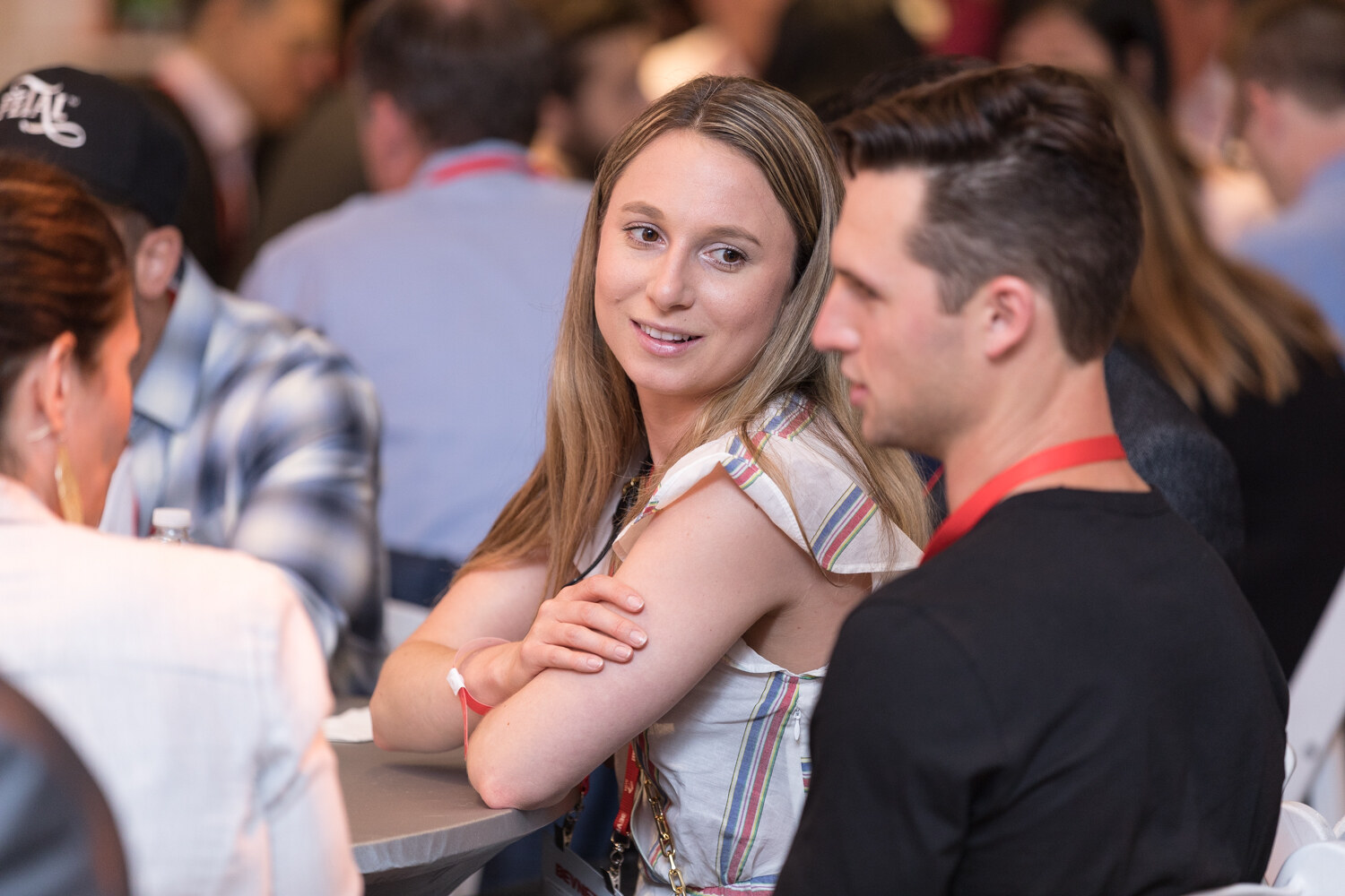 A woman and a man in lanyards sit at a table; she smiles and looks back at him.