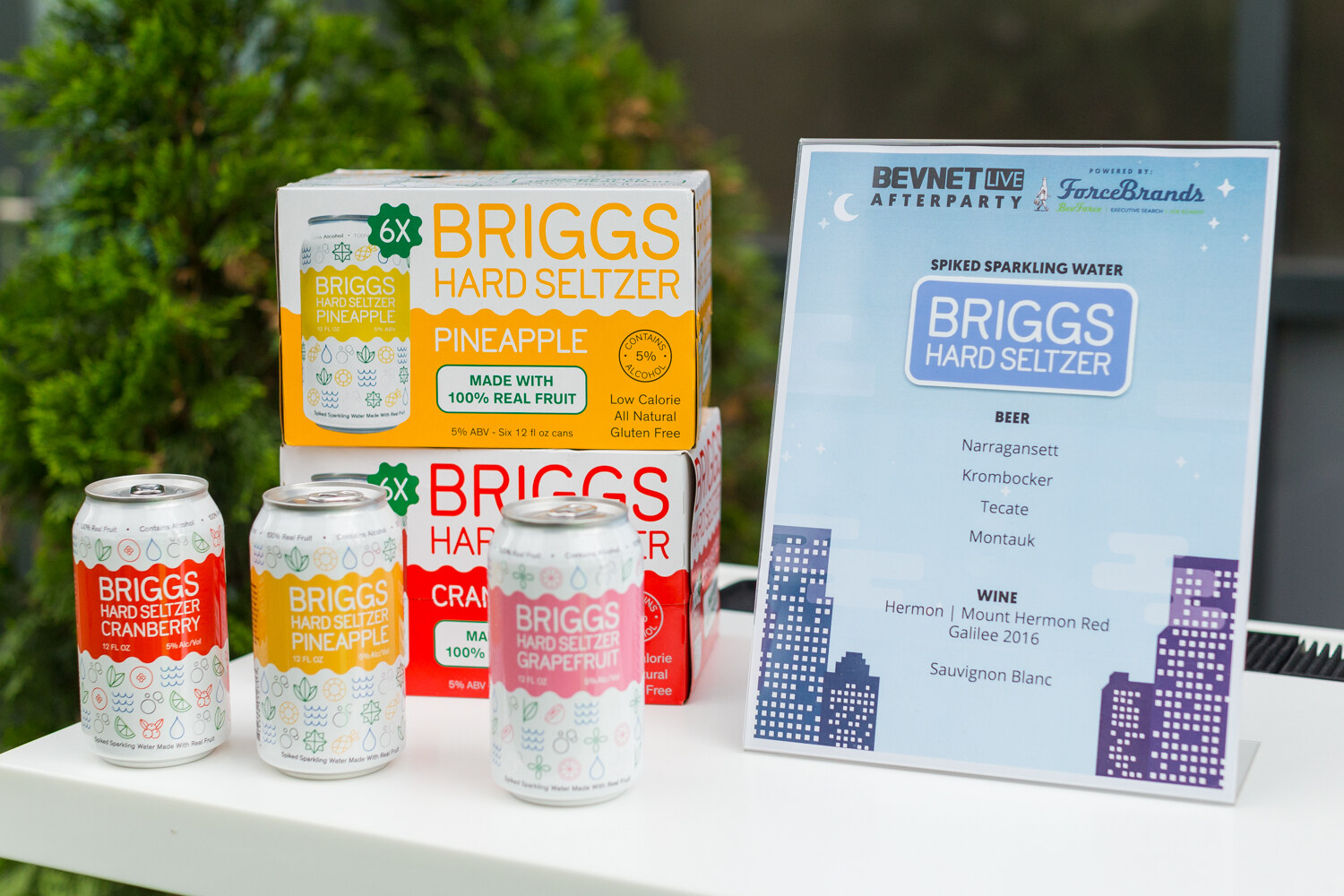 Cans and boxes of Briggs Hard Seltzer in cranberry, pineapple and grapefruit beside a sign for the BevNET Live Afterparty listing beer and wine.