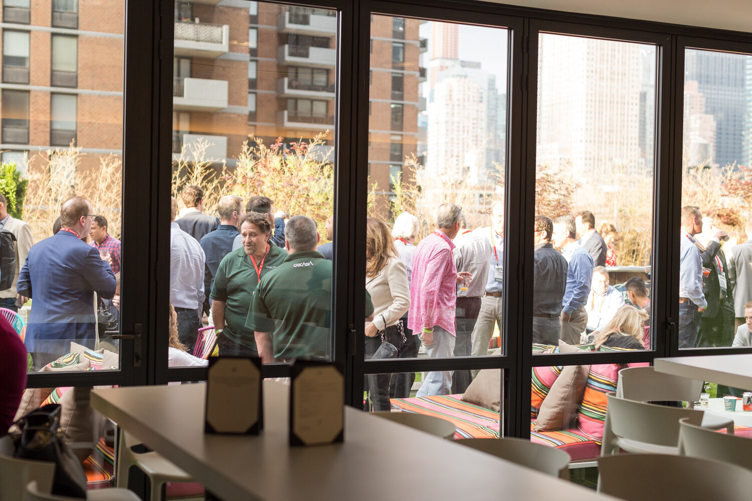View through large windows onto a crowded terrace, with a long counter and chairs inside the room.