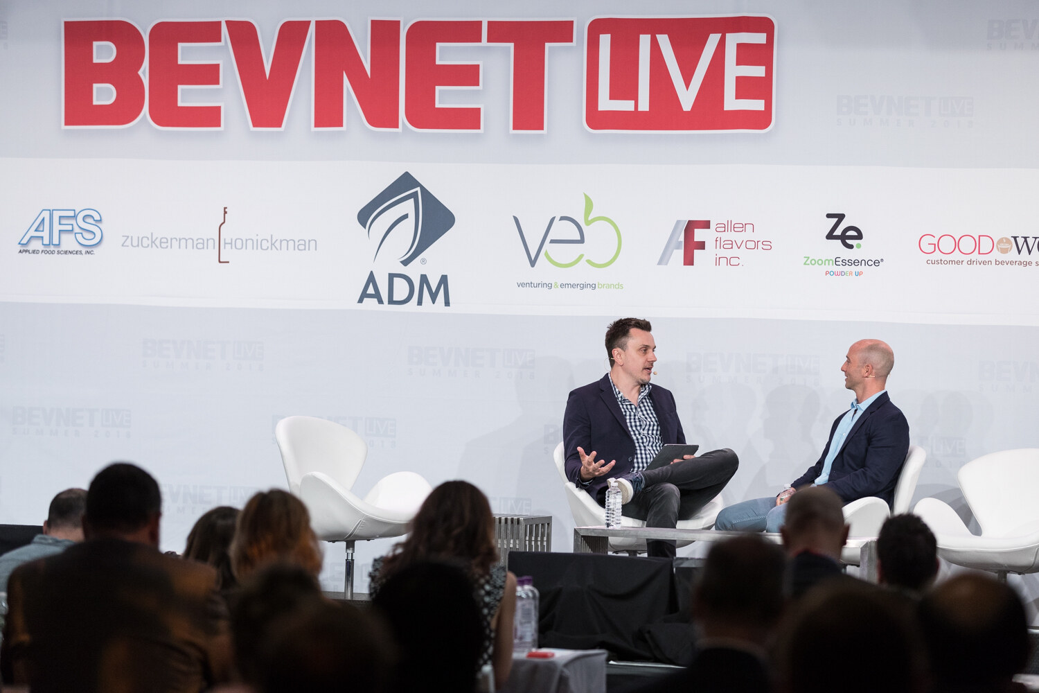 Wide view of two men seated on stage in front of the BevNET Live sign with an audience in the foreground.