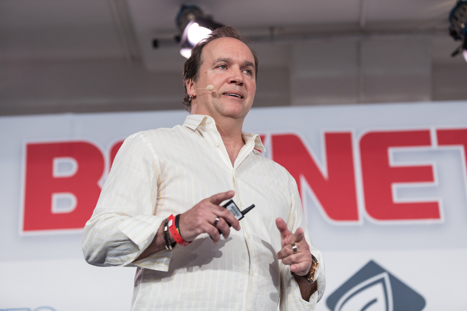 A man in a cream open-collar shirt holds a clicker and gestures in front of the BevNET Live sign.