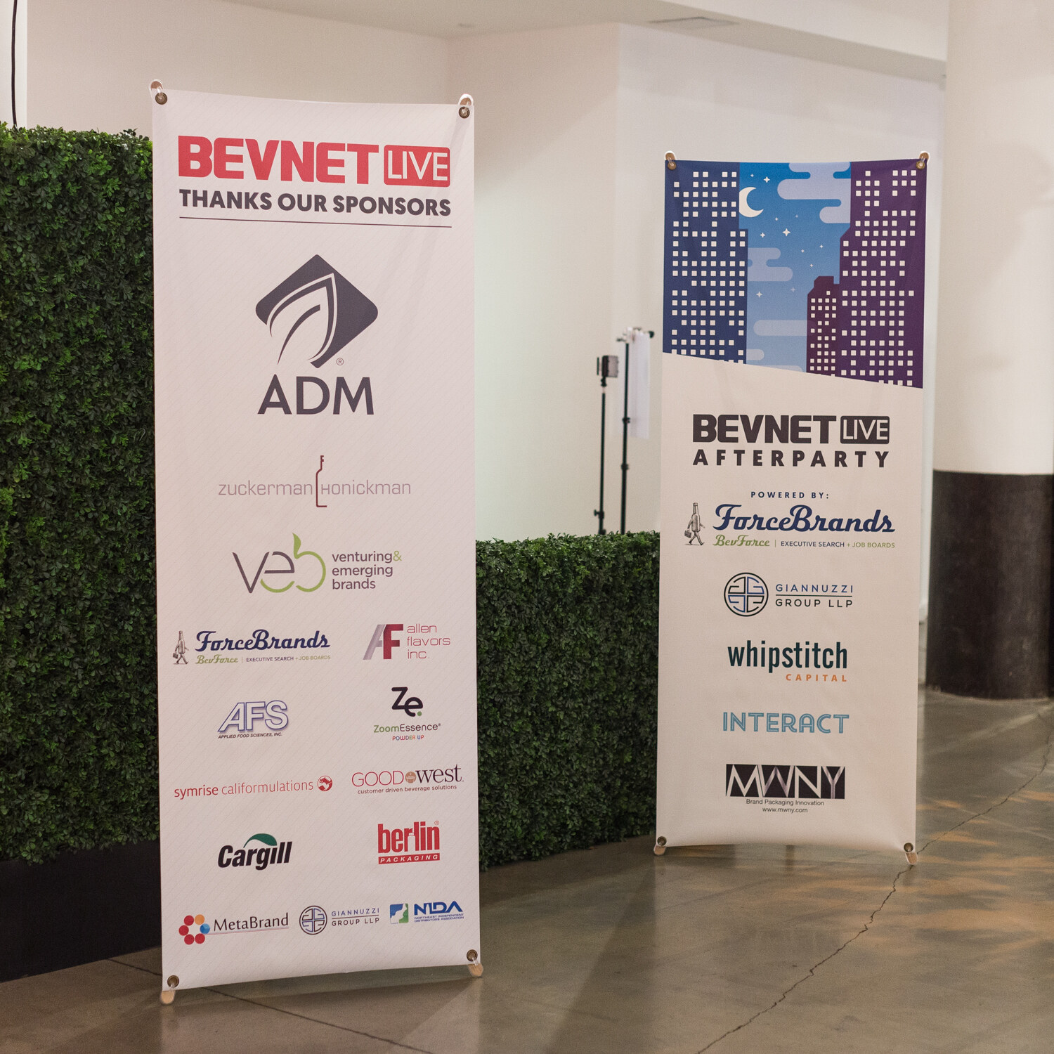 Two banners beside a hedge wall, one reading BevNET Live Thanks Our Sponsors with ADM and others, the other for the BevNET Live Afterparty powered by ForceBrands.