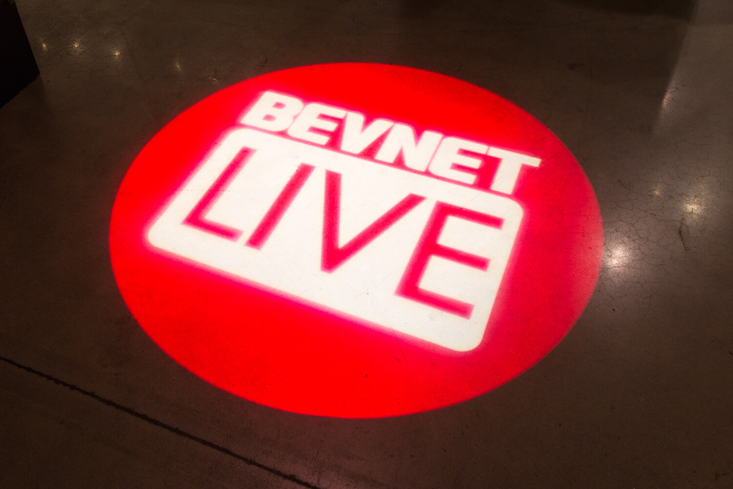 A red circle on a dark floor containing the white BevNET Live logo.