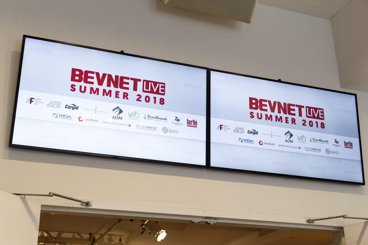 Two wall-mounted screens showing BevNET Live Summer 2018 with sponsor logos including ADM, Veb and Cargill.