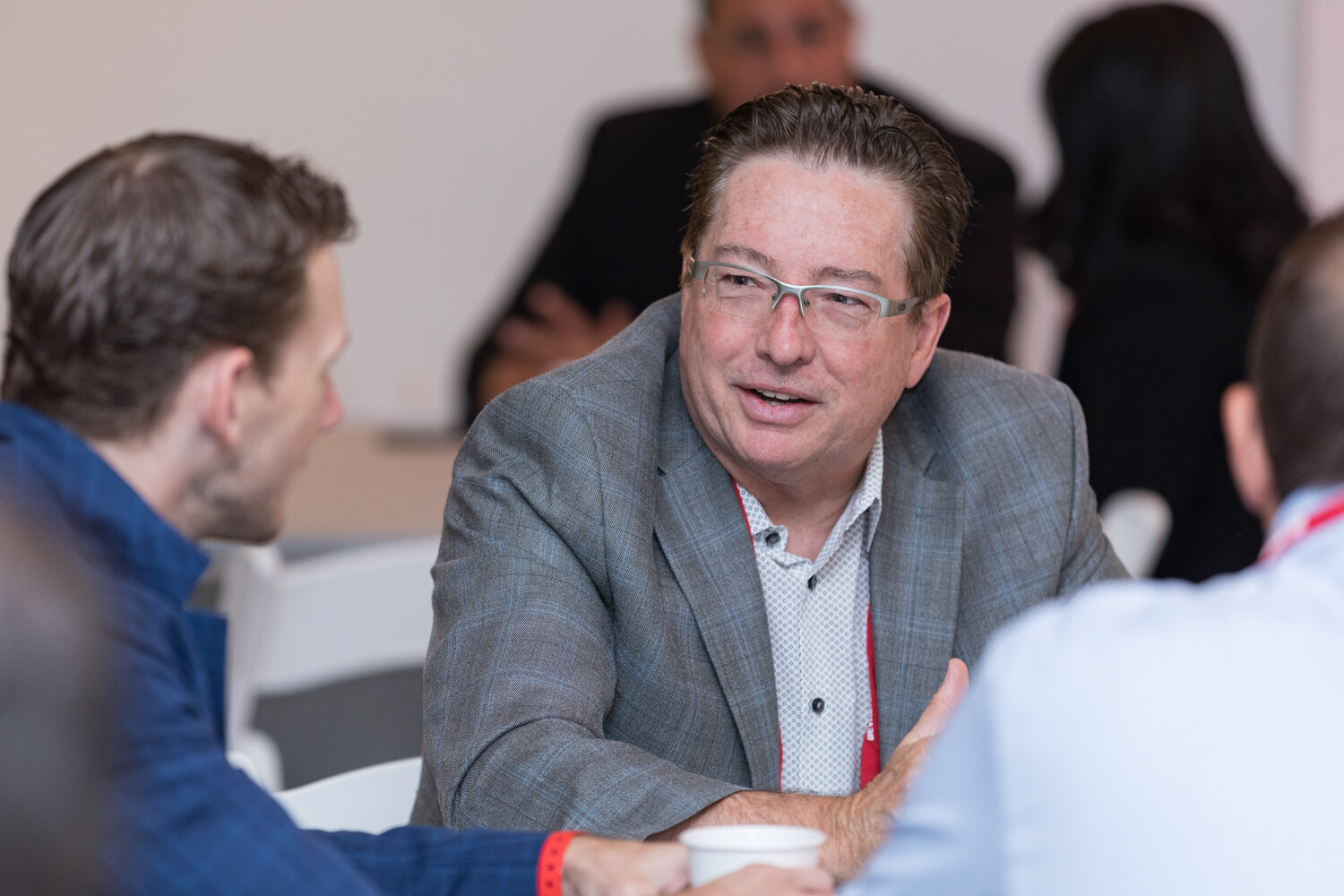 Smiling attendee in a gray blazer chatting at a round table.