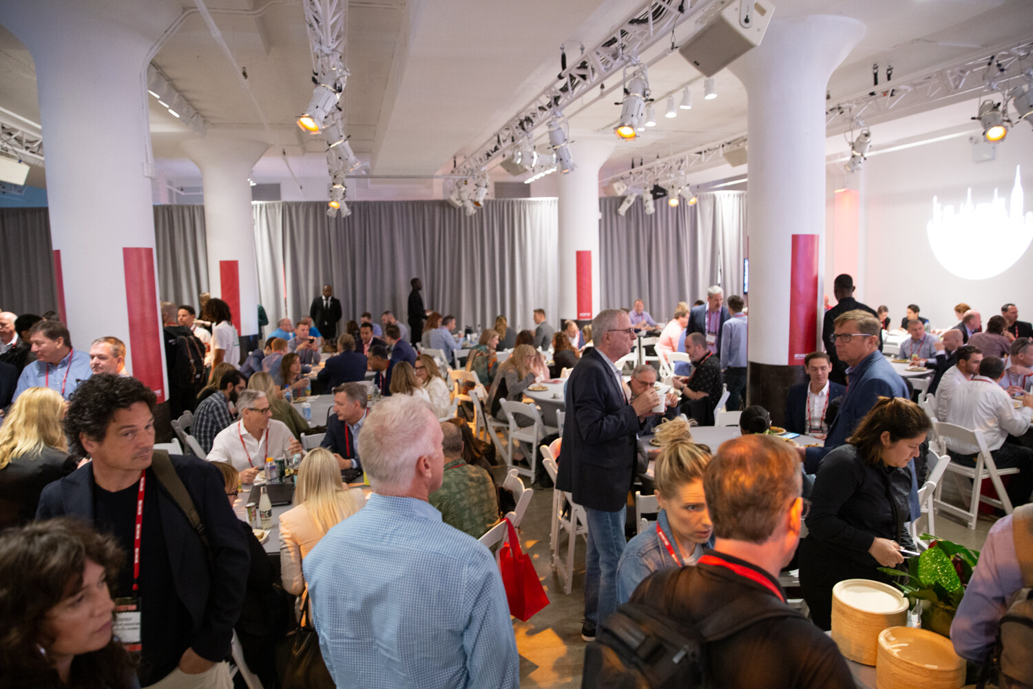 Wide view of attendees seated at round tables in the networking space.