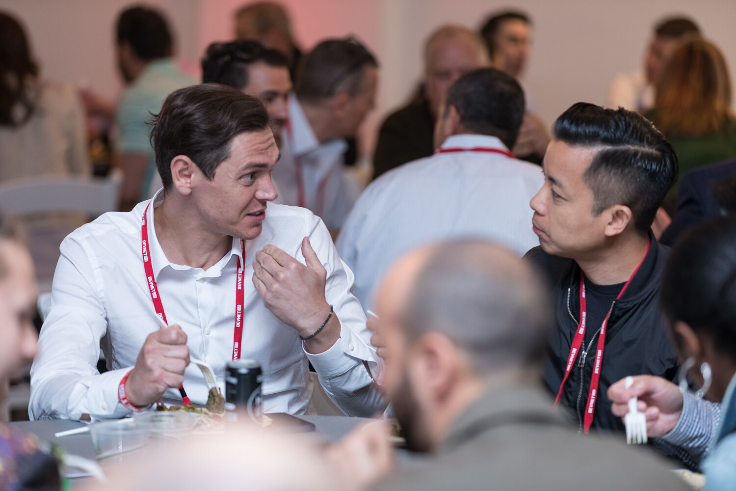 Two attendees talking over lunch at a crowded round table.
