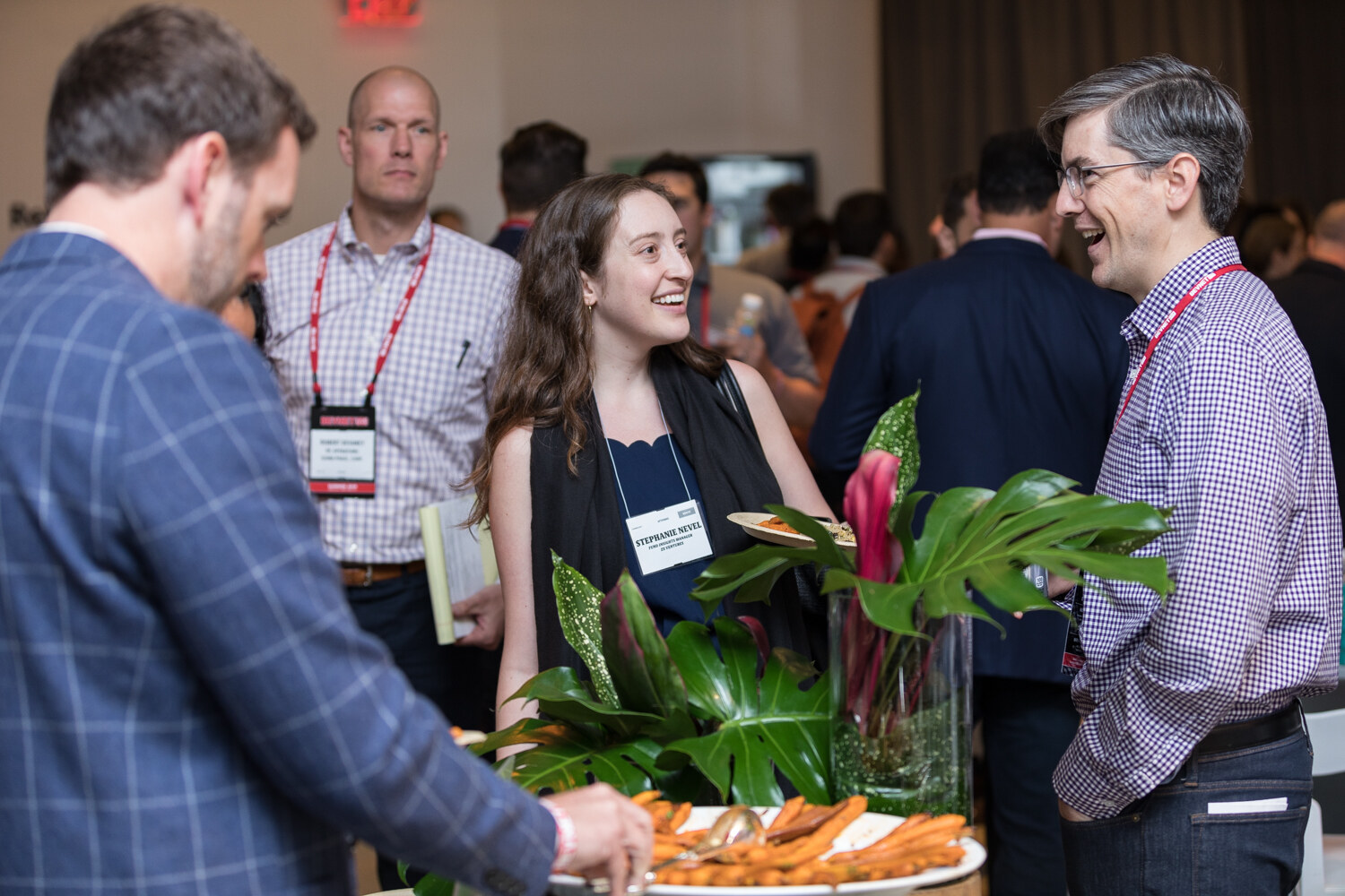 Attendees chatting beside a buffet table with tropical plants.