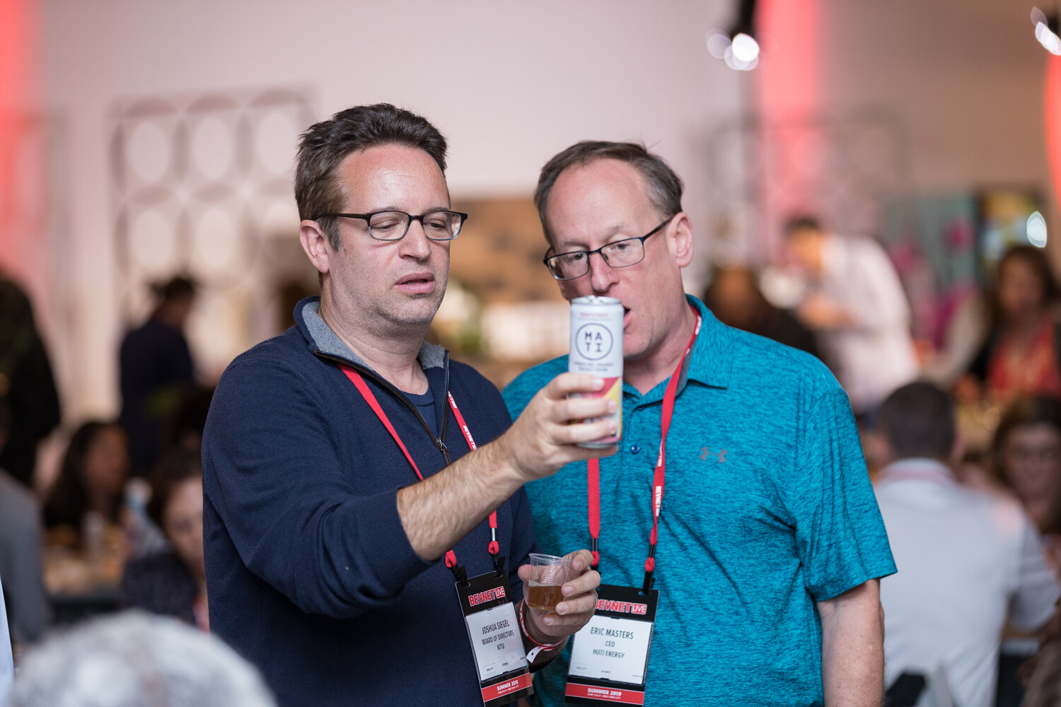Two attendees comparing a white can while holding sample cups.