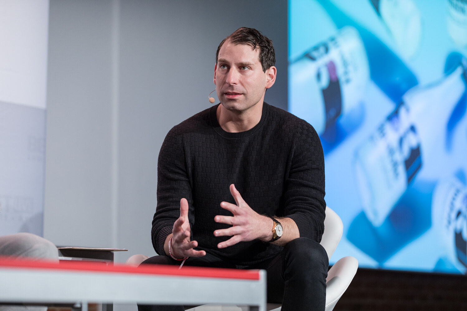 Judge in a black sweater gesturing with both hands in front of a slide of blue bottles.