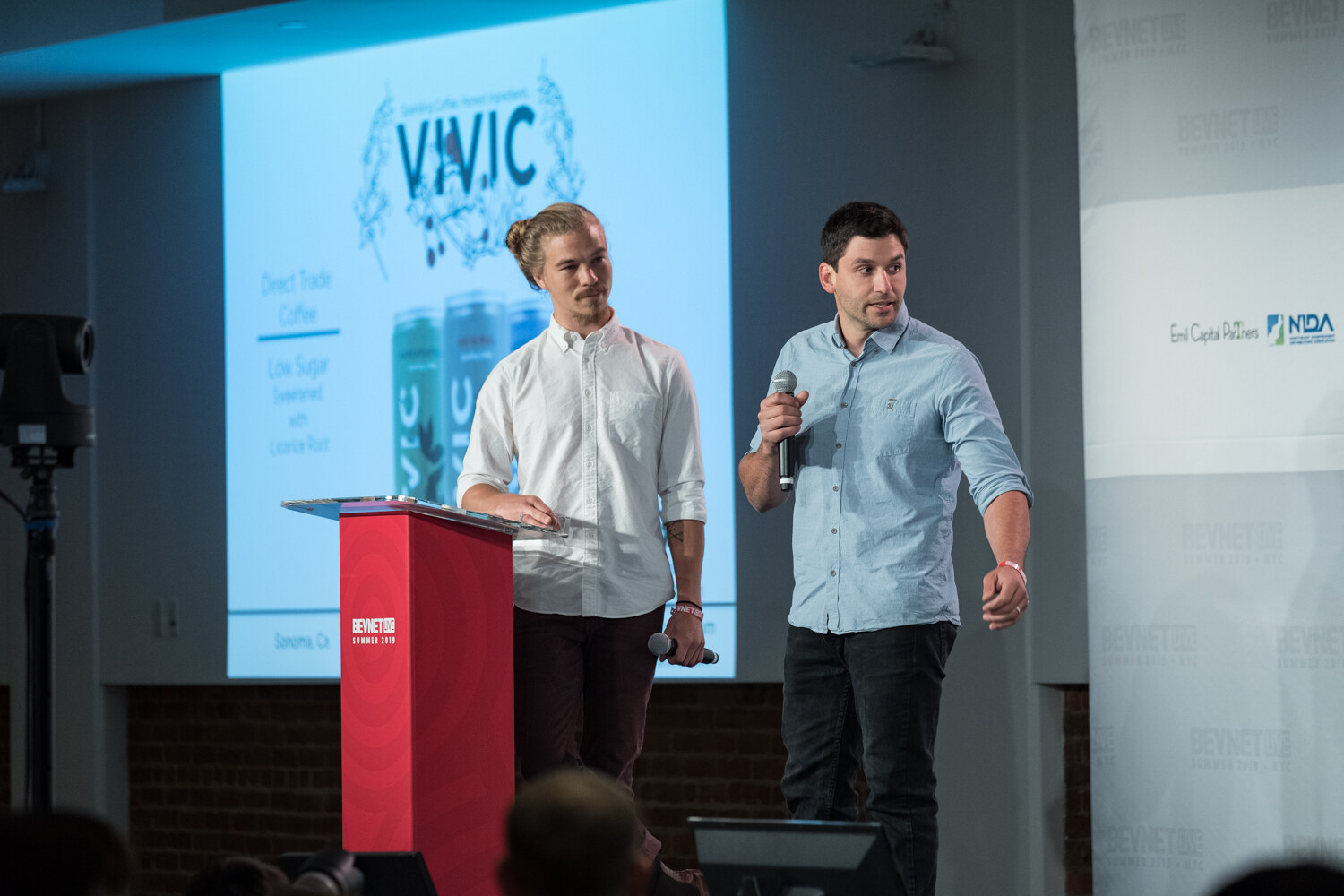 Two men at the red podium in front of a slide for VIVIC.