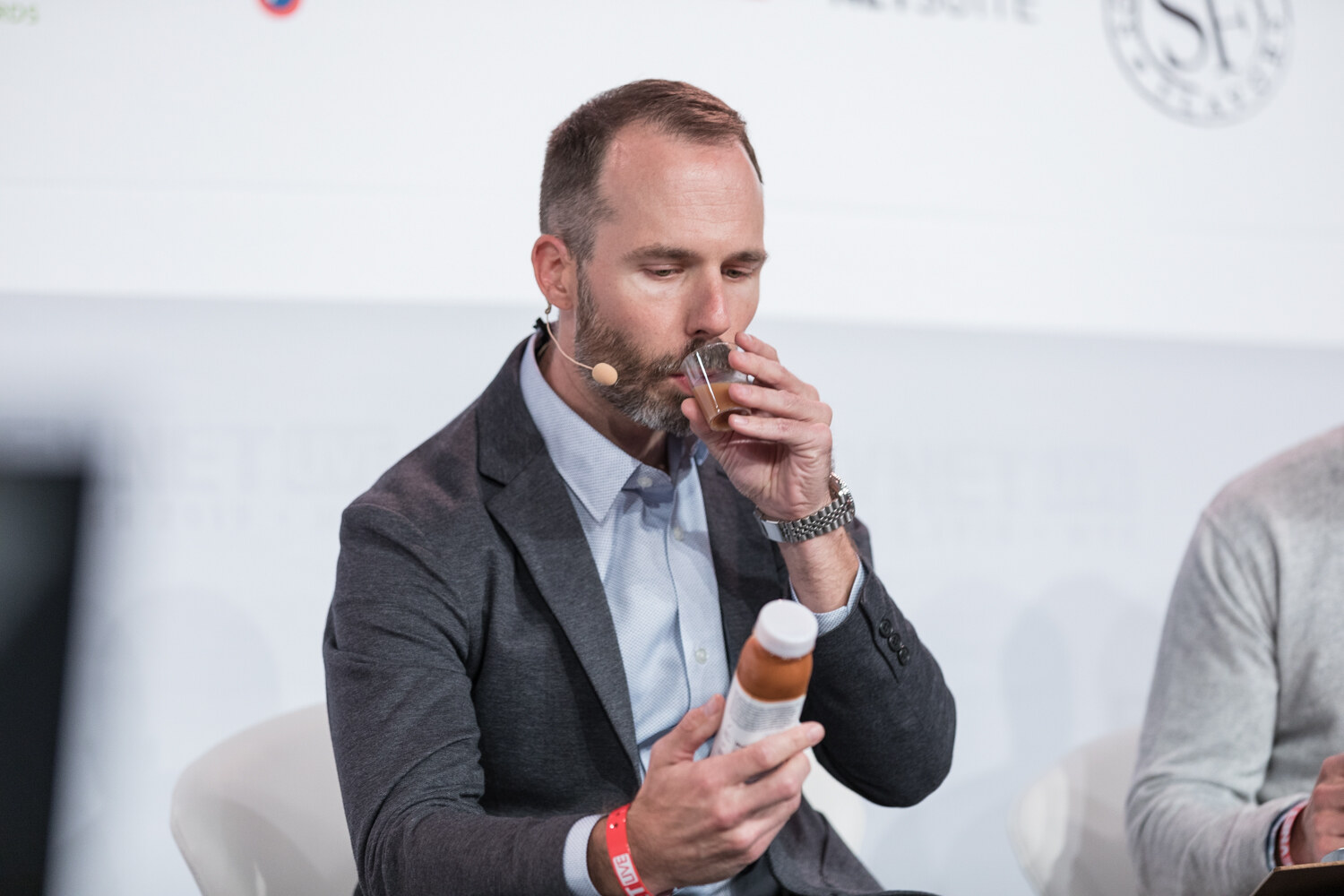 Judge in a gray blazer smelling a sample from a bottle.