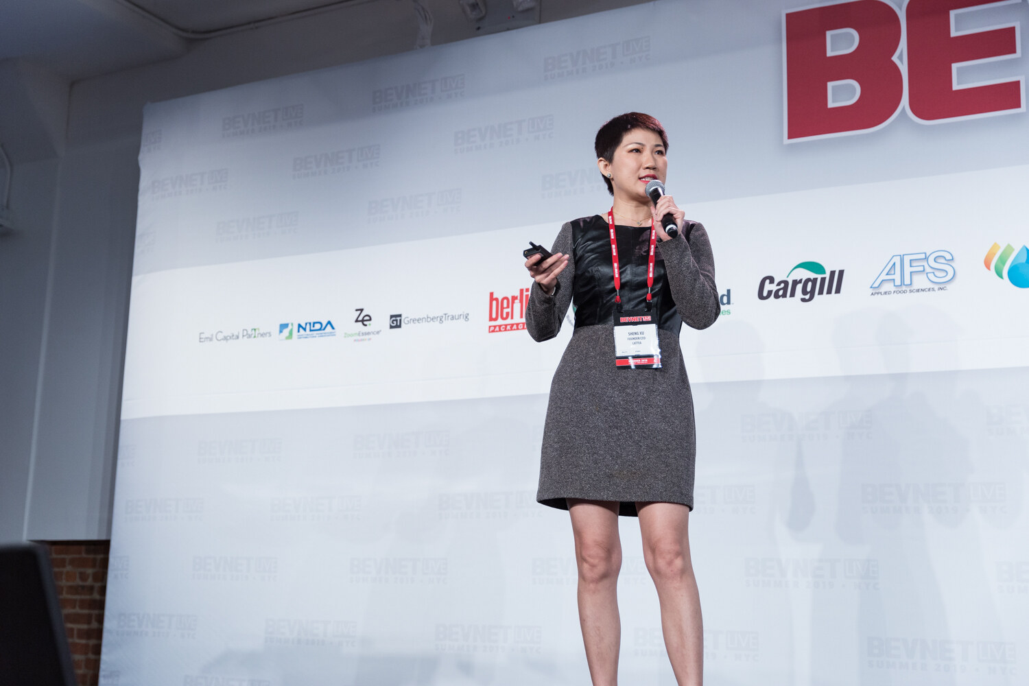 Woman in a gray dress and BevNET lanyard speaking into a microphone in front of Berlin Packaging, Cargill and AFS signs.
