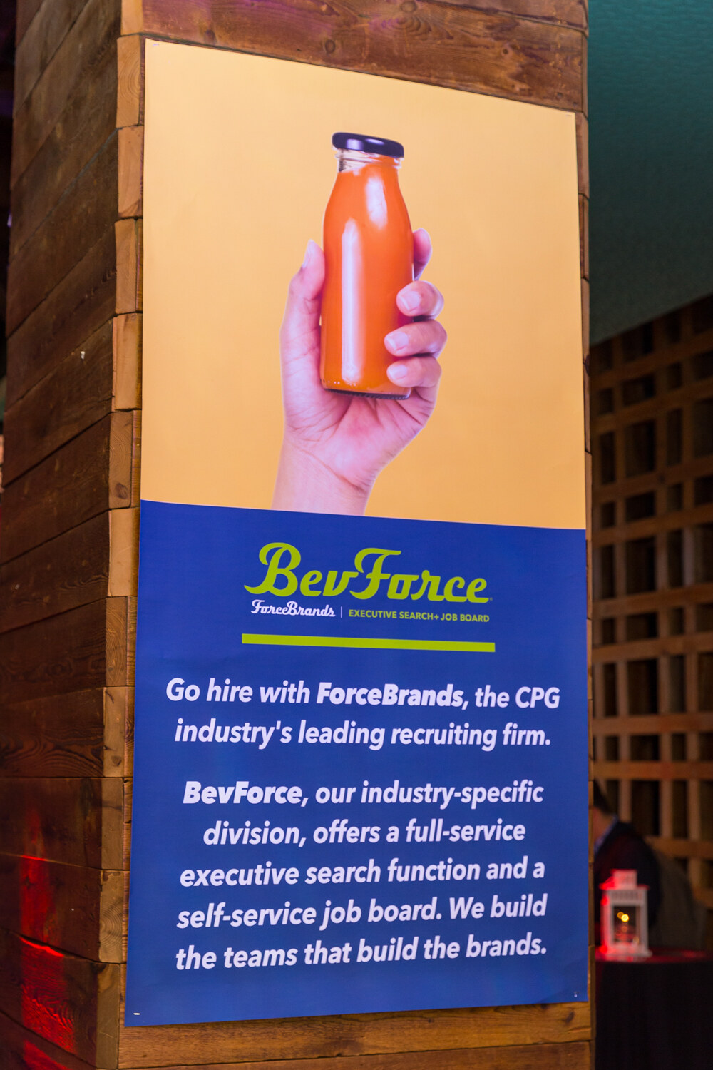 BevForce poster inviting guests to hire through ForceBrands, with a hand holding an orange juice bottle.