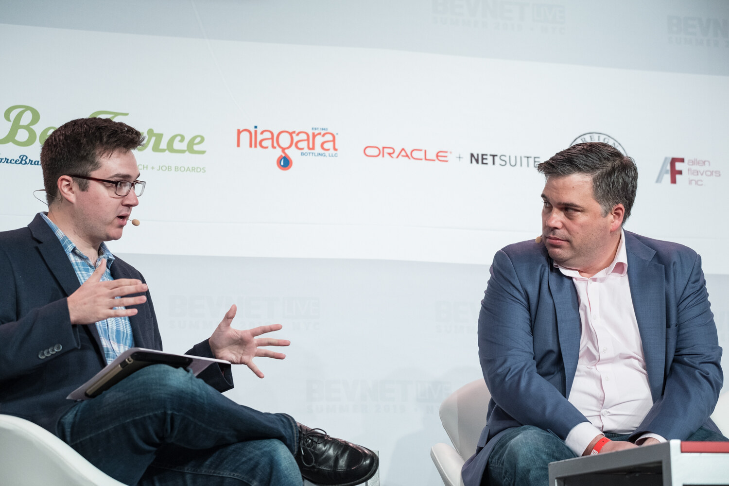 Interviewer in glasses and a plaid shirt and a man in a blue blazer seated in white chairs in front of BevForce and Niagara logos.