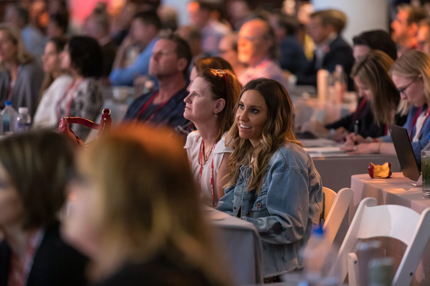 Smiling woman in a denim jacket seated among attendees at a session table.