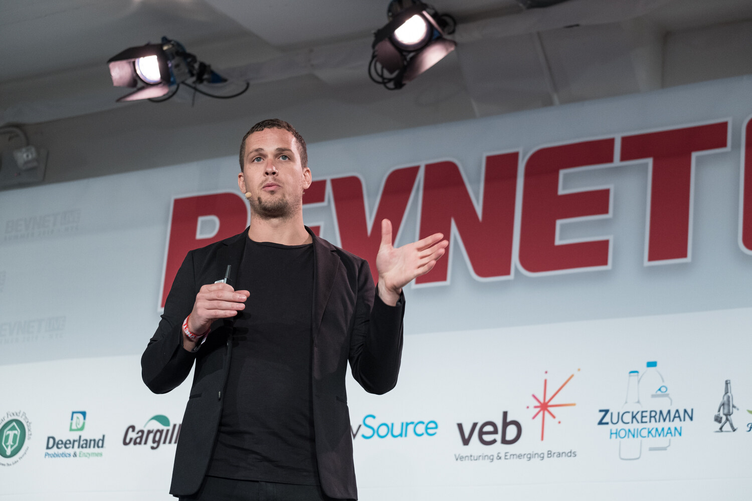 Speaker in a black blazer with his hand out in front of the BevNET sign.