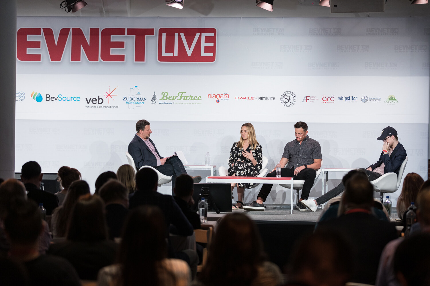 Wide view of the four-person panel on the BevNET Live stage with the audience in silhouette in the foreground.