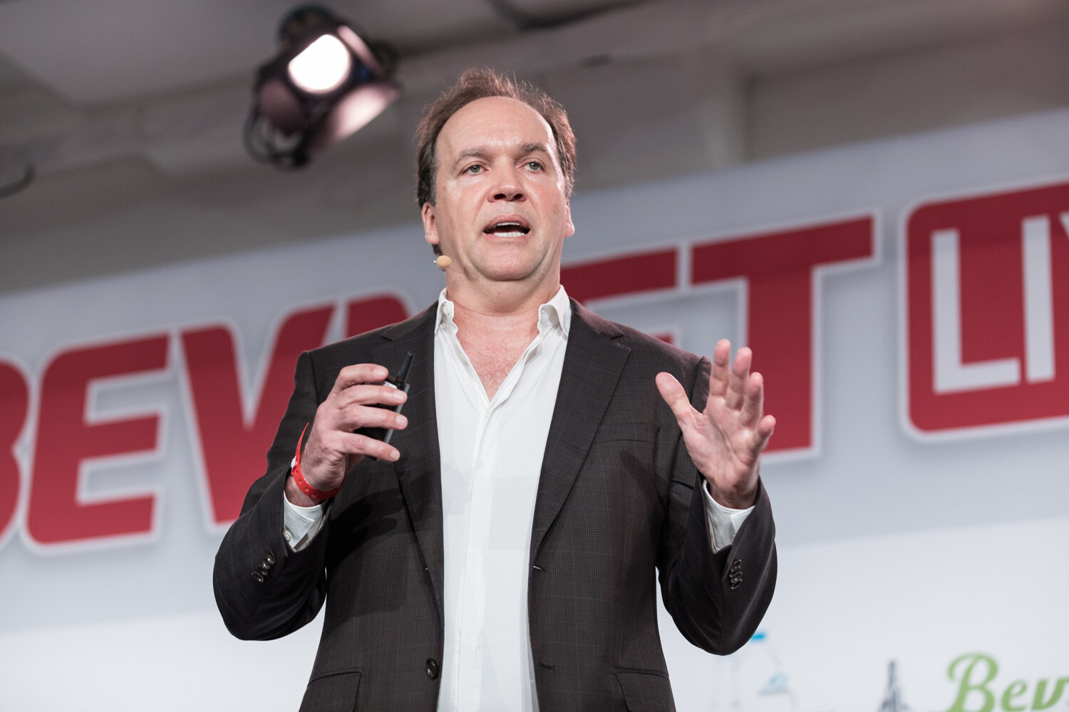 Speaker in a dark blazer with both hands raised in front of the BevNET Live sign.