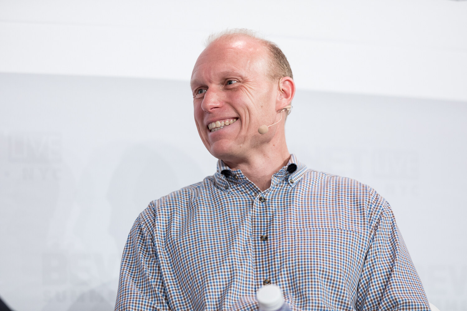 Smiling seated speaker in a checked shirt.