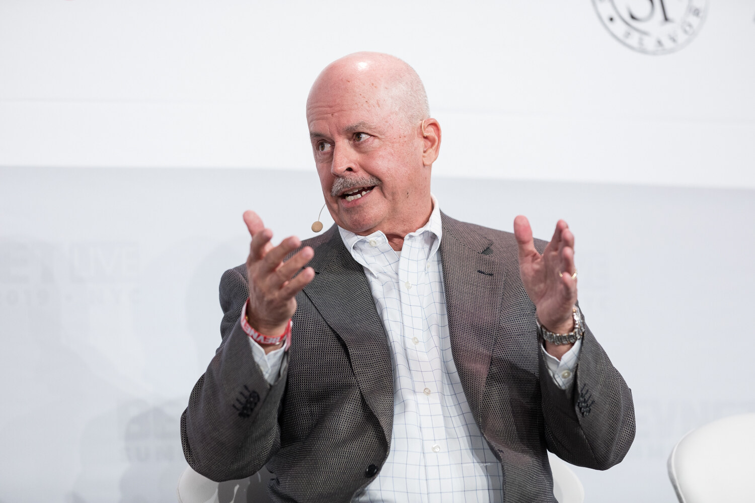 Seated guest in a gray blazer gesturing with both hands.