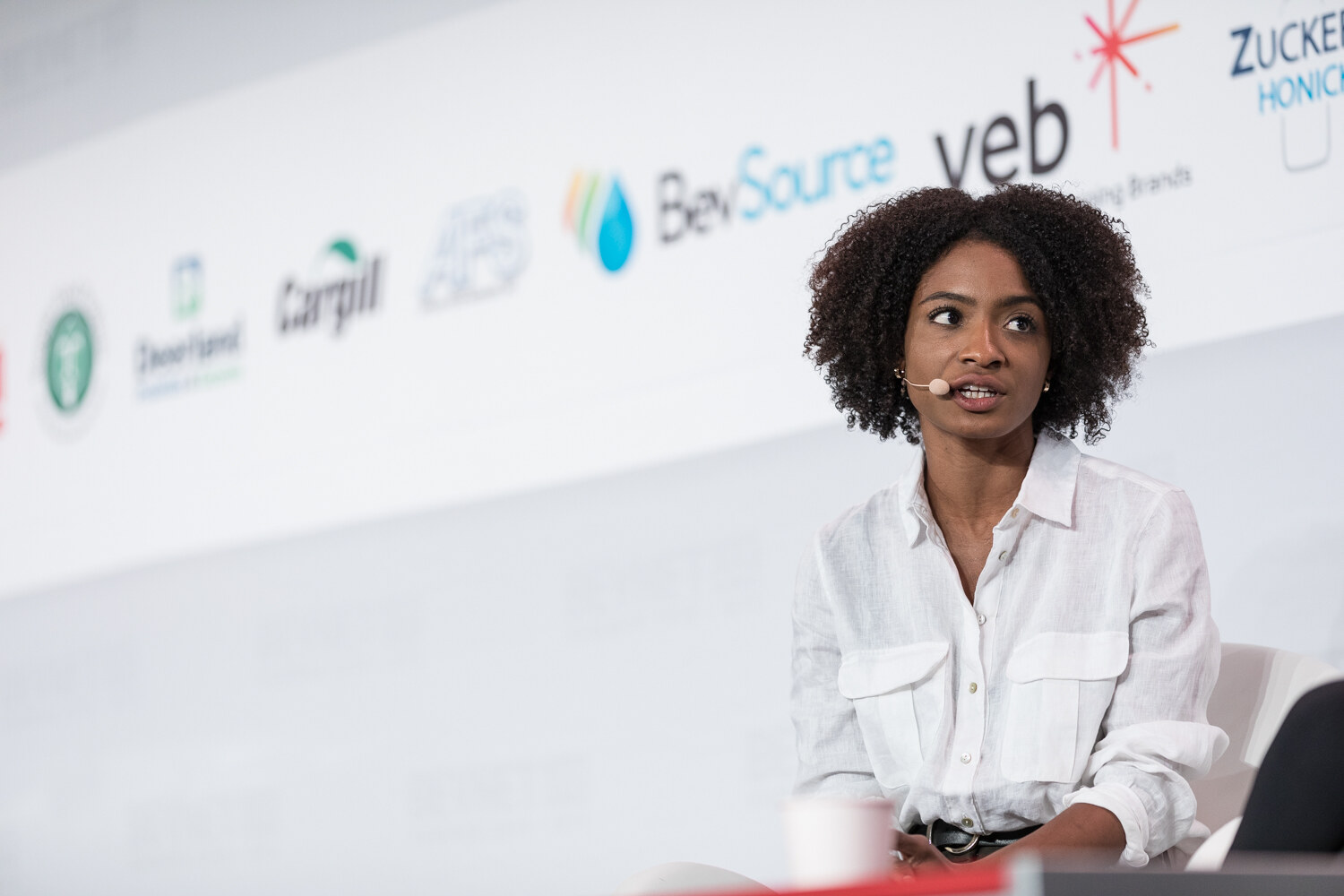Woman in a white linen shirt seated on stage in front of Deerland, Cargill, BevSource and veb logos.