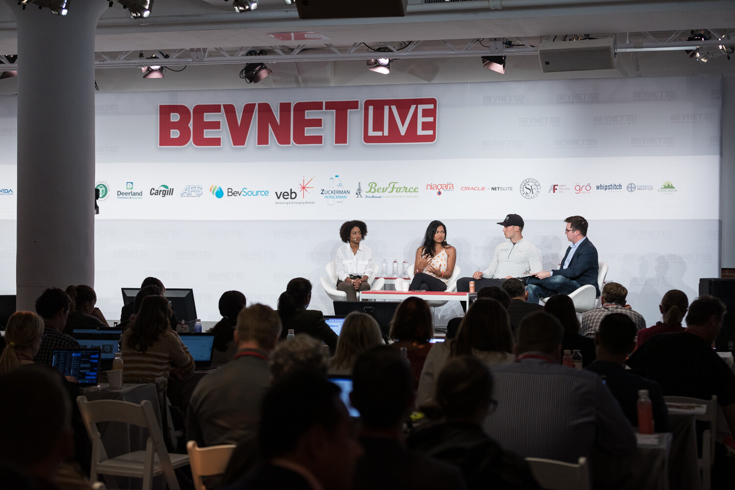 Wide view of the panel on stage with attendees at laptops in the foreground.