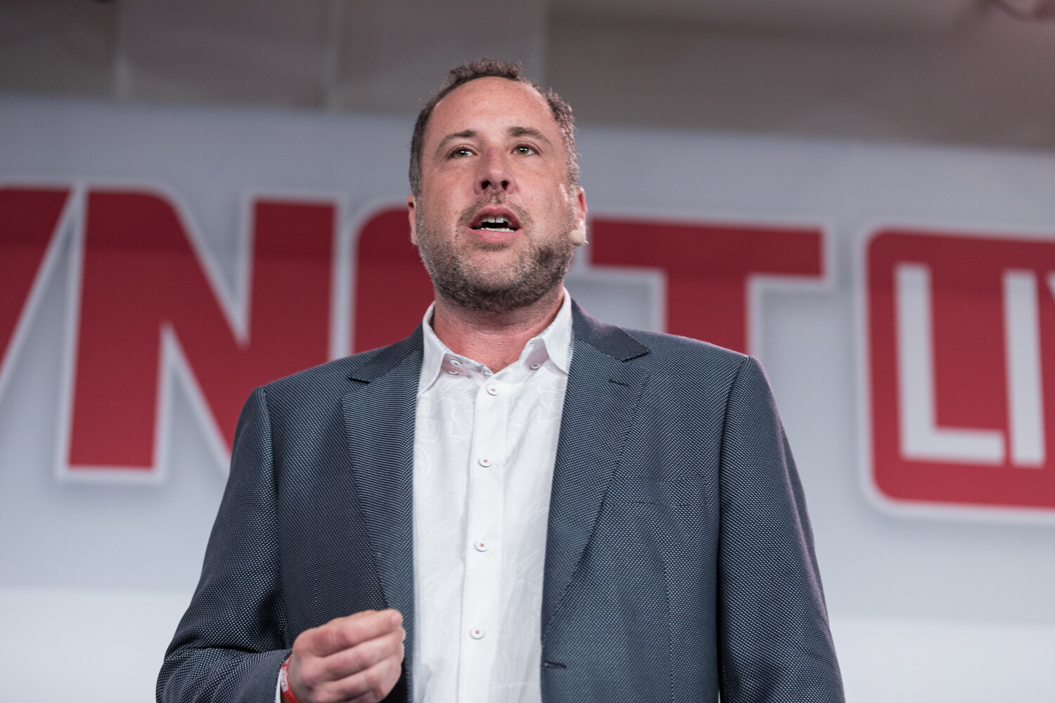 Close view of a man in a gray blazer and white shirt speaking in front of the BevNET Live logo.