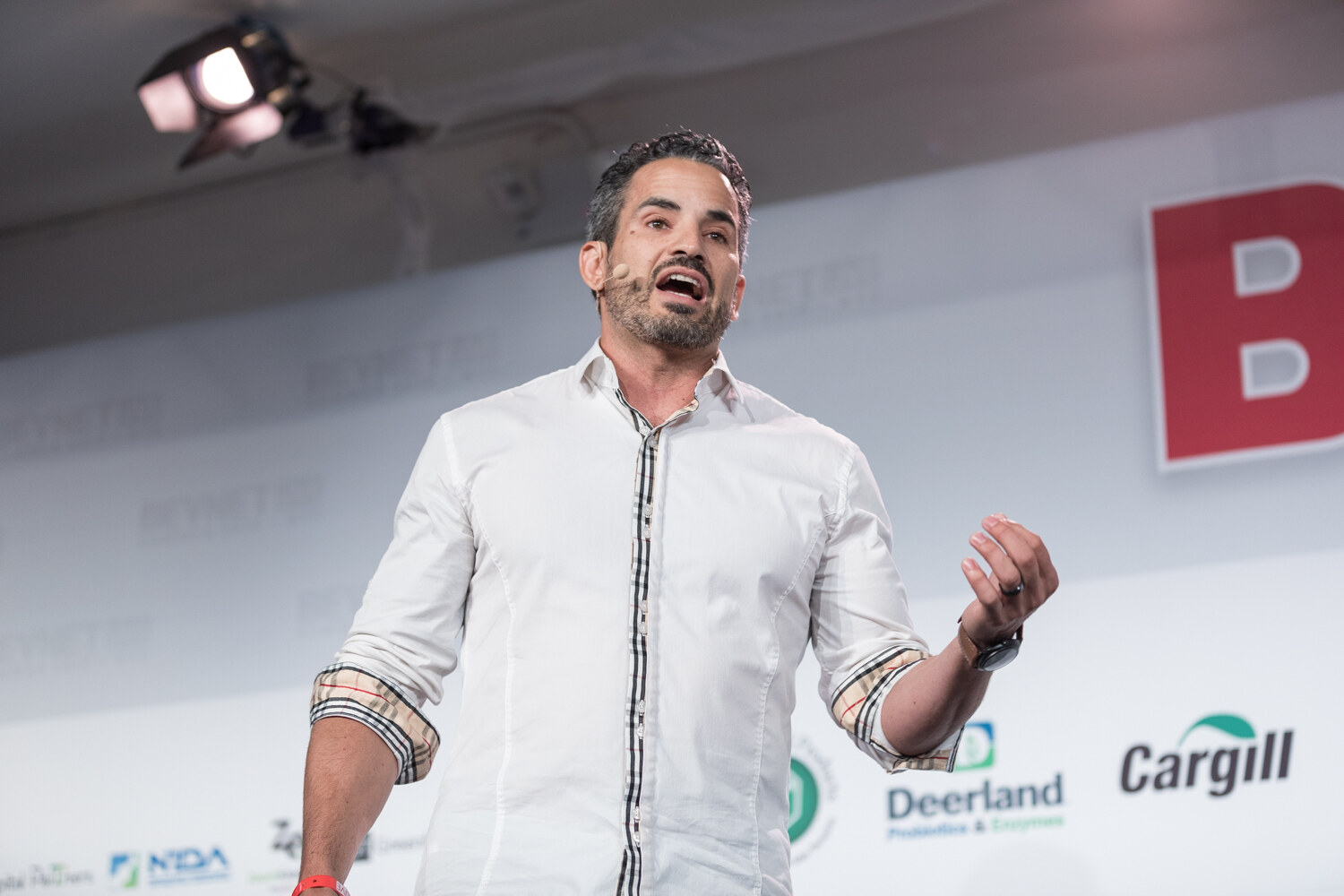 Man in a white shirt with plaid cuffs gesturing in front of Deerland and Cargill logos.