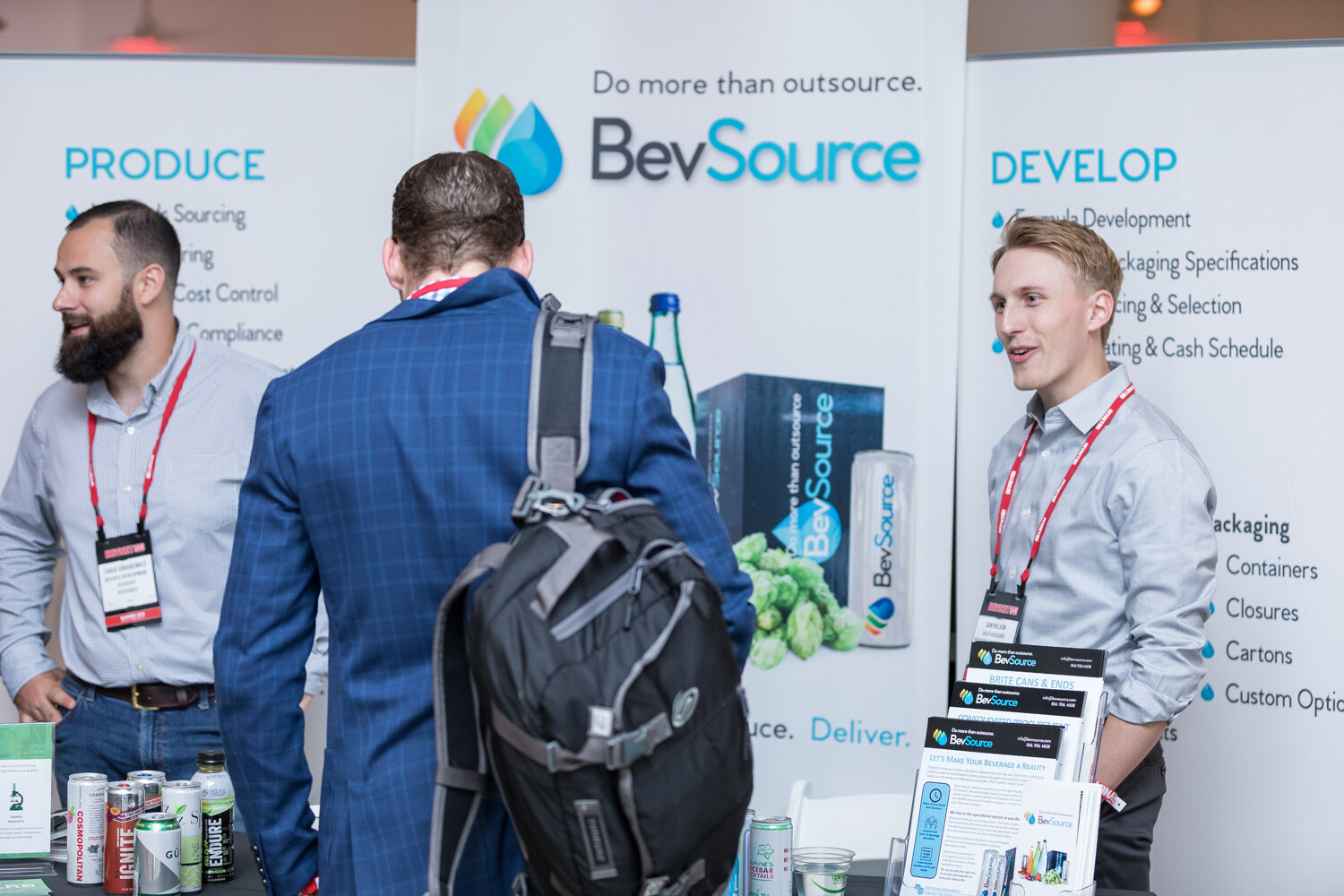 Attendees at the BevSource booth in front of a display of beverage cans and hops.