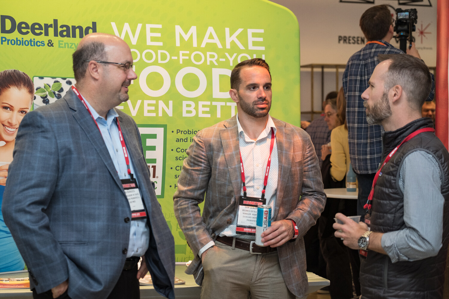 Three attendees chatting in front of a green Deerland Probiotics and Enzymes banner.