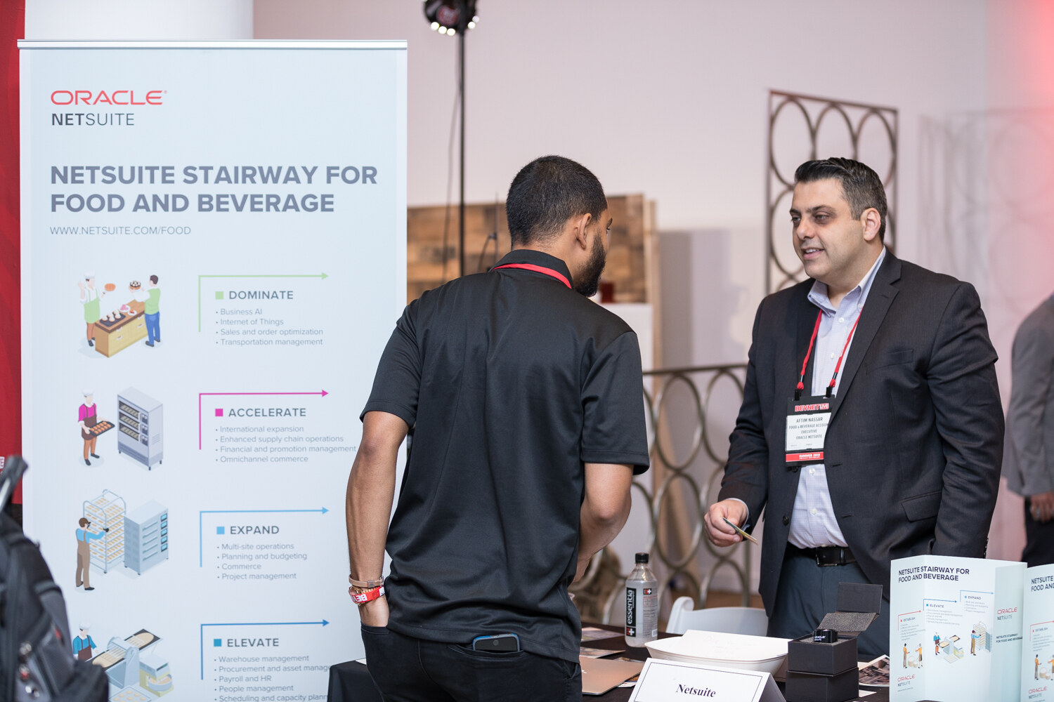 Attendees at the Oracle NetSuite booth beside a banner titled NetSuite stairway for food and beverage.