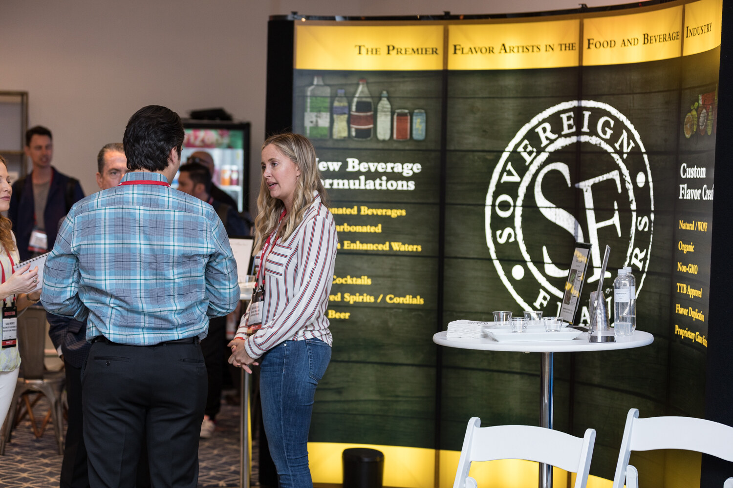 Attendee talking with a woman at the Sovereign Flavors display with its new beverage formulations sign.
