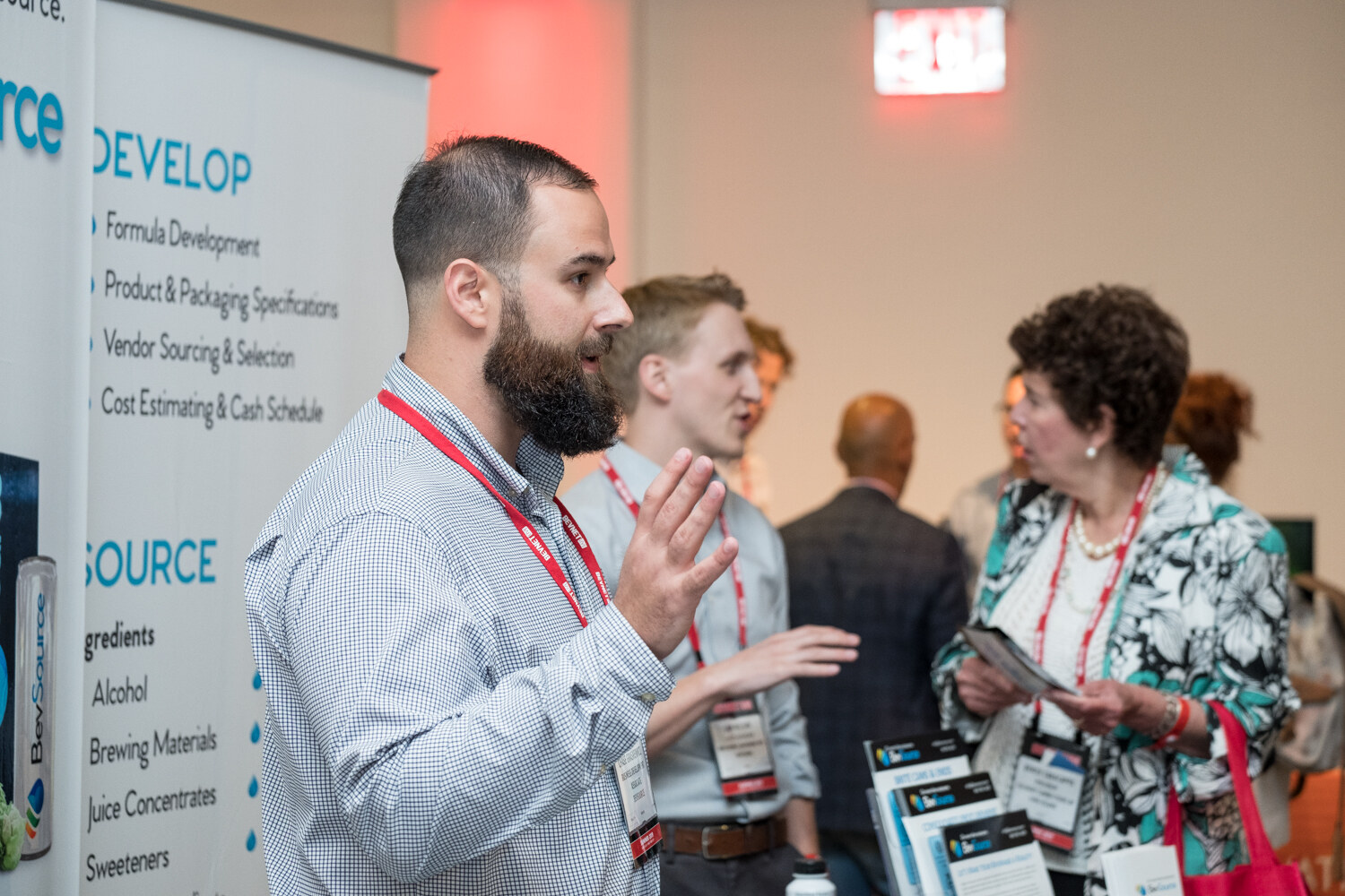 Attendees talking in front of a BevSource banner listing Develop, Produce and Deliver services.