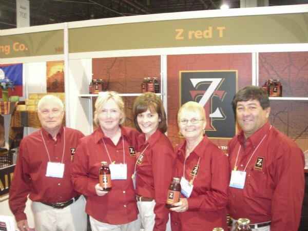 Five people in matching red shirts and badges, including Jack Scimeca, Deborah Pelleria, Doren Scimeca, Judy Scimeca and Gil Pellerin of Z Red Tea, hold bottles at their booth.