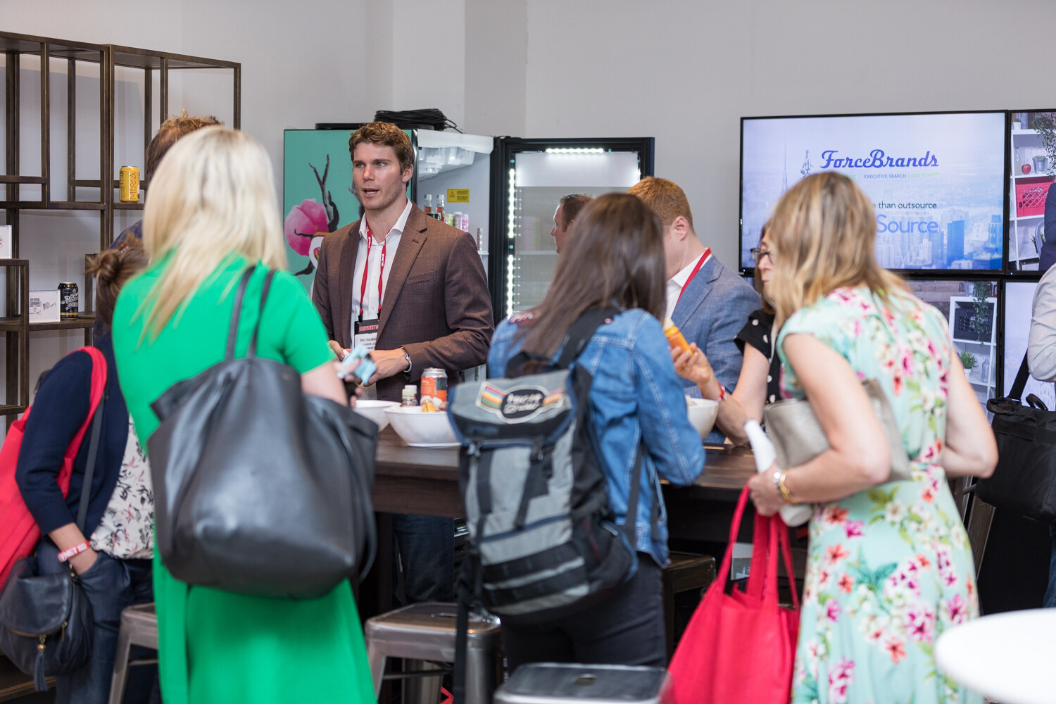 Attendees gathered around a ForceBrands display with a lit screen and a refrigerated cooler.