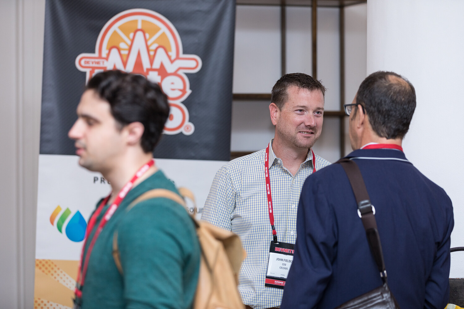 Attendees talking in front of a banner with an orange logo and a BevSource drop.