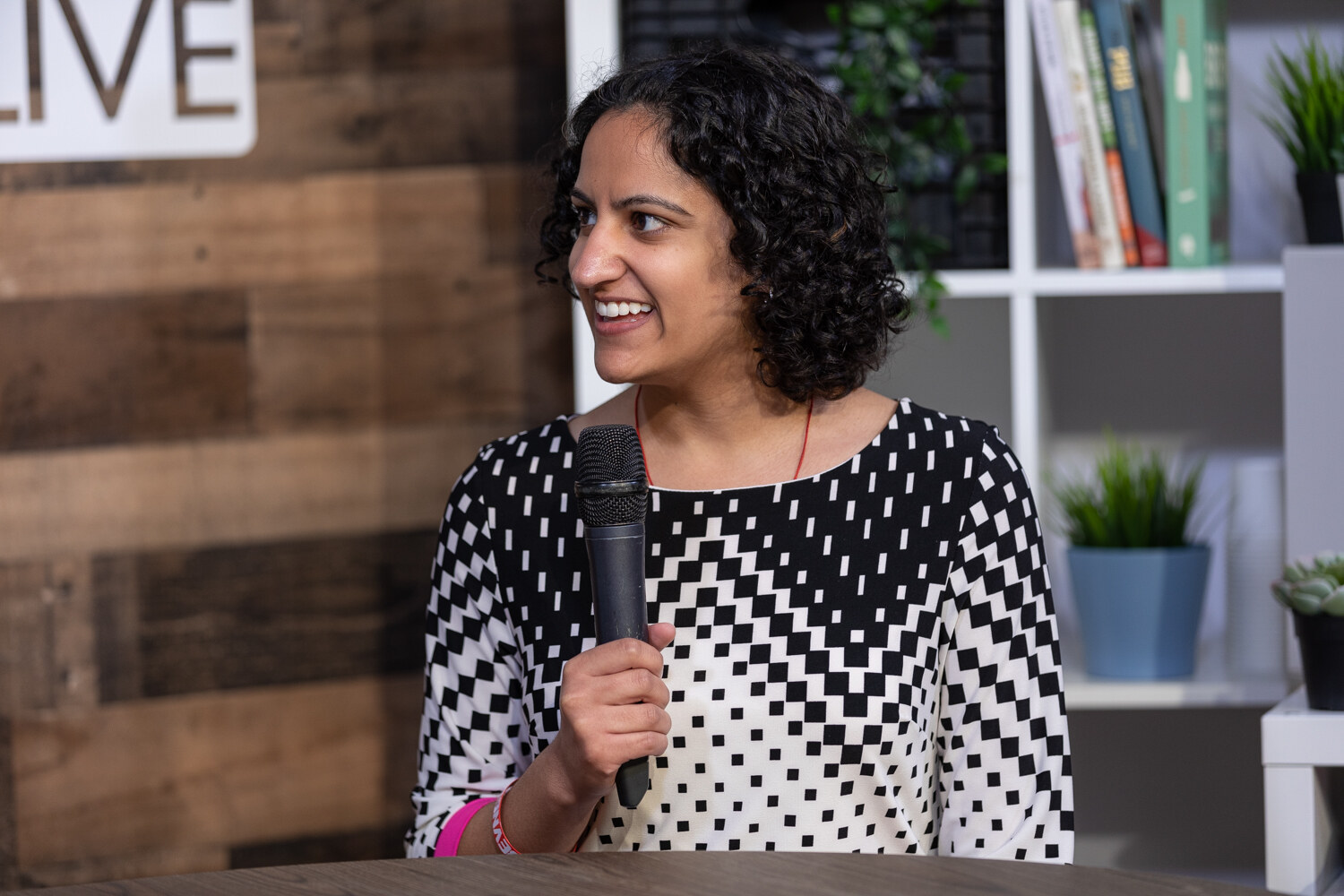 Smiling woman with curly dark hair in a black and white pixel-print top at the livestream set.