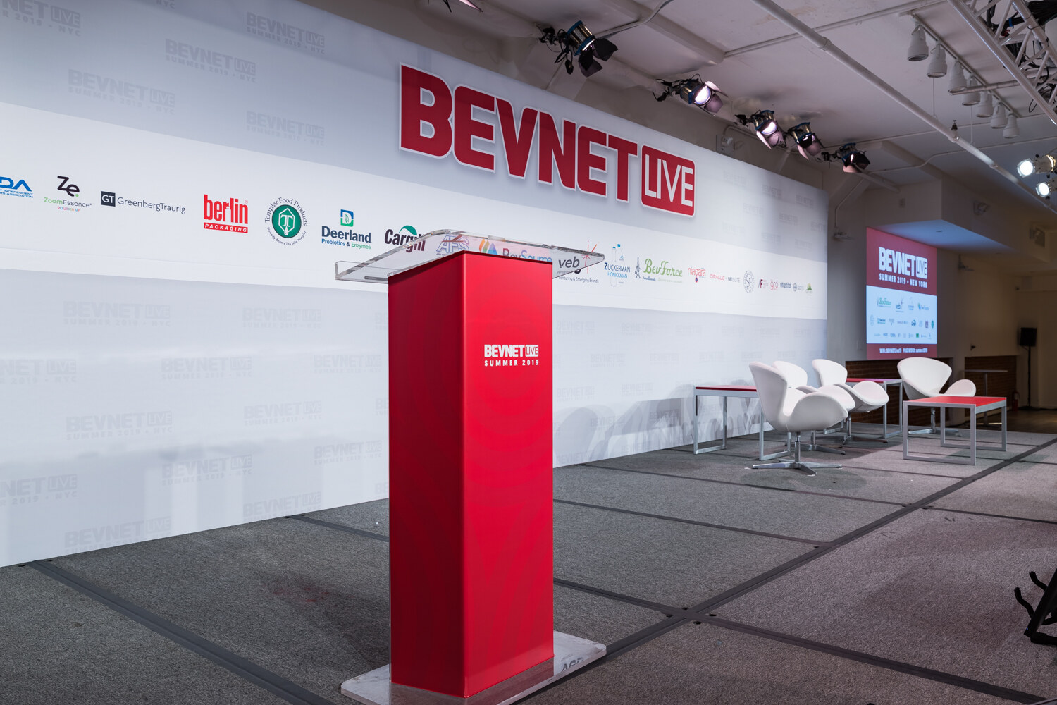 Red BevNET Live podium and white lounge chairs on the empty main stage.