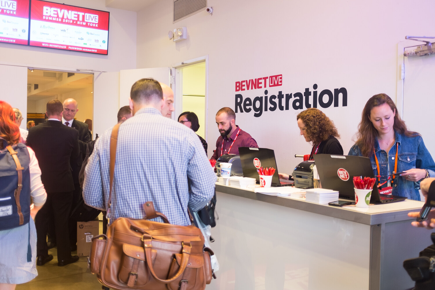 BevNET Live Registration wall above the check-in desk as arriving attendees wait.