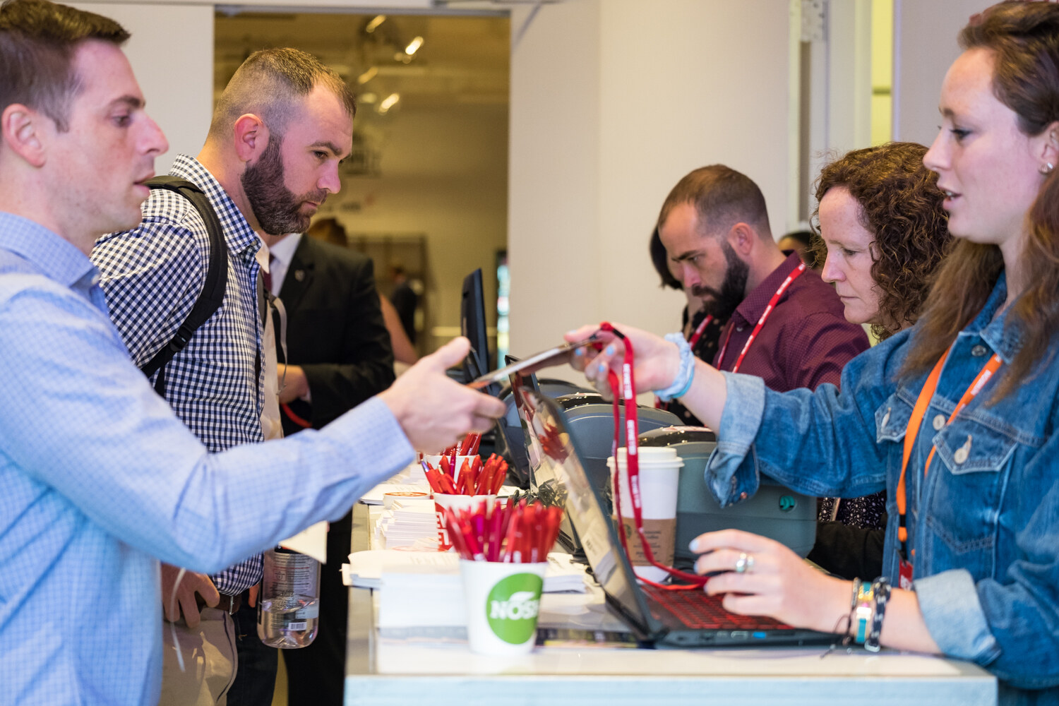 Attendee receiving a lanyard from a registration staffer, with a green Nosh cup of red pens on the counter.